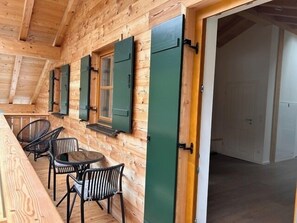 Une cabane en bois comprenant un coin repas avec une table et des chaises, une porte et une fenêtre avec des volets.