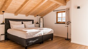 Una camera da letto con soffitto in legno, un letto con lenzuola bianche, un comodino, una lampada da terra e una finestra con tende.