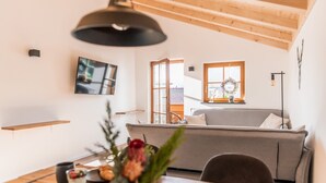 Un accogliente soggiorno con un divano grigio, travi a vista in legno, un televisore a schermo piatto montato a parete e un tavolo da pranzo con un vaso di fiori.