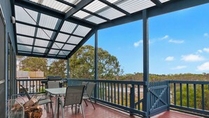 A covered outdoor deck with a table and chairs, a grill, and a metal rack with logs. - Chez Reeve - 6 National Park Road, Loch Sport (Loch Sport)