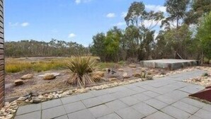 A paved patio area with a stone border, surrounded by natural vegetation and trees. - Chez Reeve - 6 National Park Road, Loch Sport (Loch Sport)