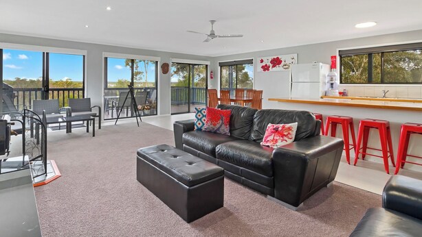 A spacious living area with a black leather sofa, red stools, and a dining table. - Chez Reeve - 6 National Park Road, Loch Sport (Loch Sport)