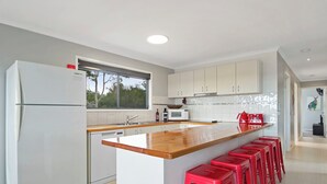 A modern kitchen with white cabinetry, a wooden island with red bar stools, a built-in oven, and a window providing natural light. - Chez Reeve - 6 National Park Road, Loch Sport (Loch Sport)