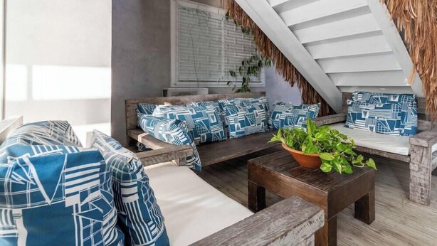 A cozy outdoor seating area with patterned cushions, a wooden table, and a potted plant. - Bossa Jurere Hotel (Florianópolis)