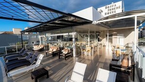 A rooftop terrace with lounge chairs, a glass-enclosed dining area, and a sign for Bossa Jurê Hotel. - Bossa Jurere Hotel (Florianópolis)