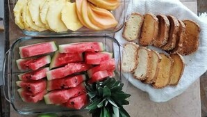 Une table sur laquelle on trouve divers aliments, notamment des tranches d’ananas, des morceaux de melon, des tranches de pomme, des morceaux de pastèque et du pain.