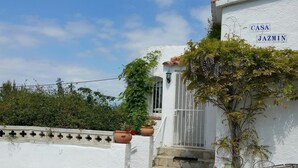 Un edificio blanco con un letrero que dice 'CASA JAZMIN' y un muro de piedra con plantas en macetas.