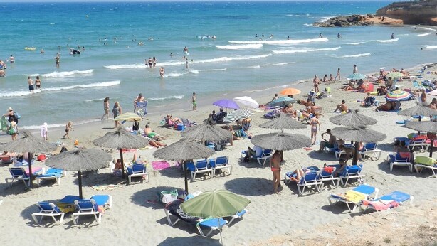 Une plage avec des transats, des parasols, et des gens qui se baignent et se promènent sur le sable.