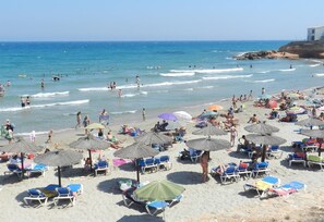 A beach with sun loungers, umbrellas, and people swimming and walking on the sand. - Apartment Playa Flamenca with Pool, A/C, Terrace & Garden (Playa Flamenca/Orihuela)