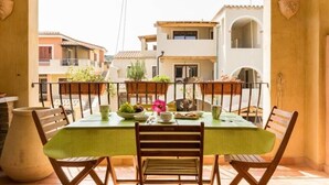 A balcony with a table set for two, surrounded by wooden chairs, with a view of neighboring buildings. - Apartment Perugino with Terrace, Balcony, A/C & Wi-Fi (Villasimius)