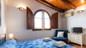 A bedroom with a bed, a TV, a dresser, and a window with shutters. - Apartment Perugino with Terrace, Balcony, A/C & Wi-Fi (Villasimius)