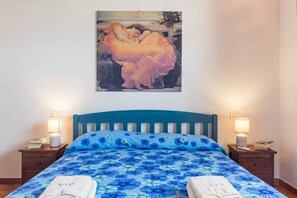 Une chambre à coucher comprenant un lit, deux tables de chevet, un tableau accroché au mur et une petite table de nuit avec une lampe.