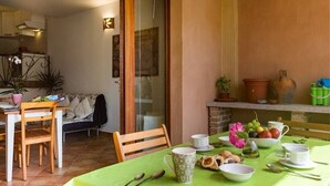 A dining area with a table set for two, chairs, a sofa, and a kitchen in the background. - Apartment Perugino with Terrace, Balcony, A/C & Wi-Fi (Villasimius)