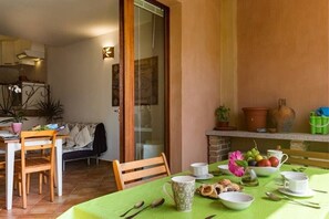A dining area with a table set for two, chairs, a sofa, and a kitchen in the background.
