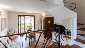 A spacious living area with a dining table, a sofa, and a staircase with a decorative railing. - Apartment Perugino with Terrace, Balcony, A/C & Wi-Fi (Villasimius)