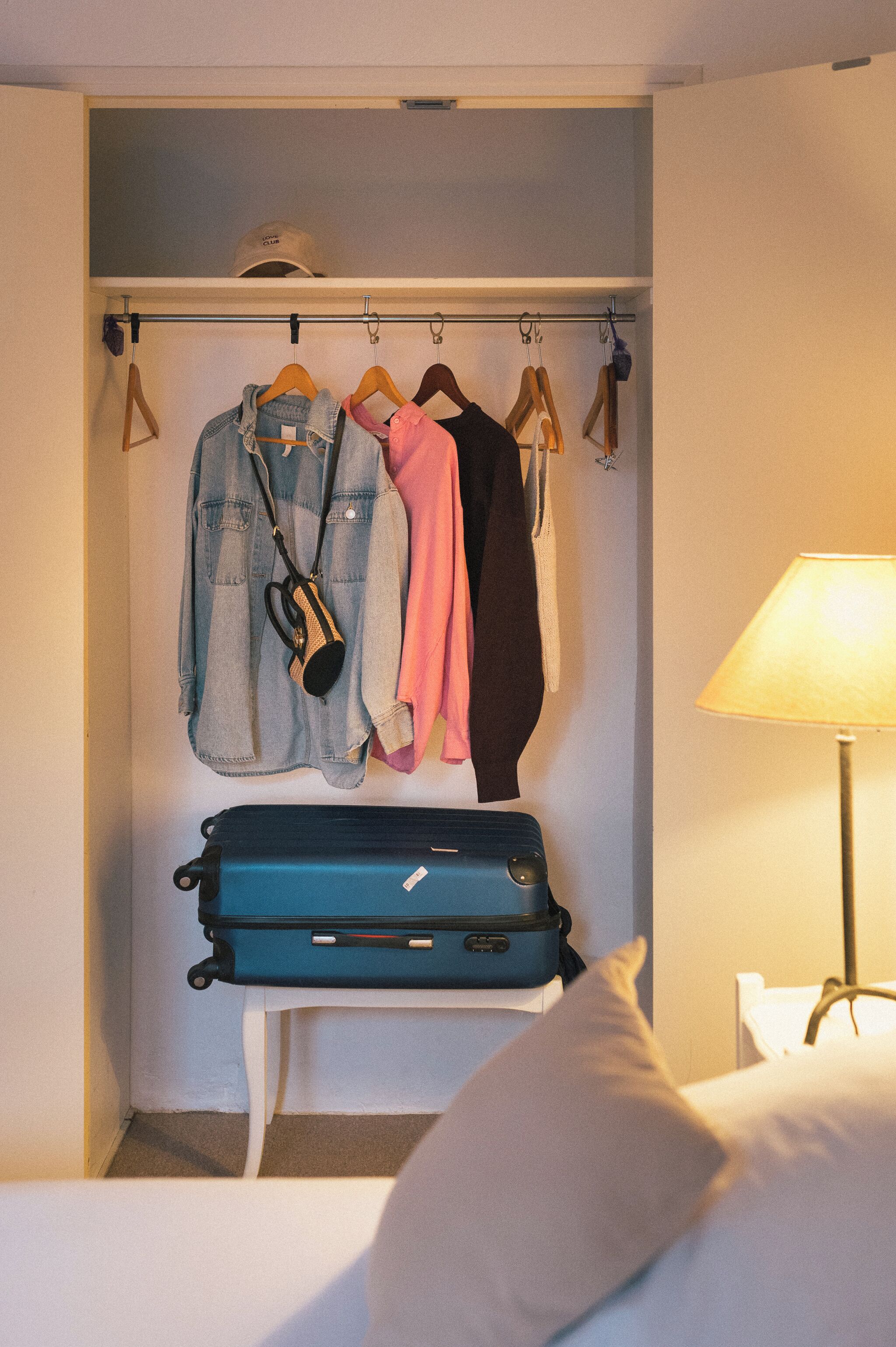 Ein Hotelzimmer mit Schrank, Kleidungsstücken zum Aufhängen und einem Koffer.