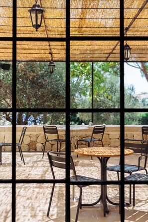An outdoor dining area with tables and chairs, a thatched roof, and a view of greenery through large windows. - Auberge du Redier (Colomars)