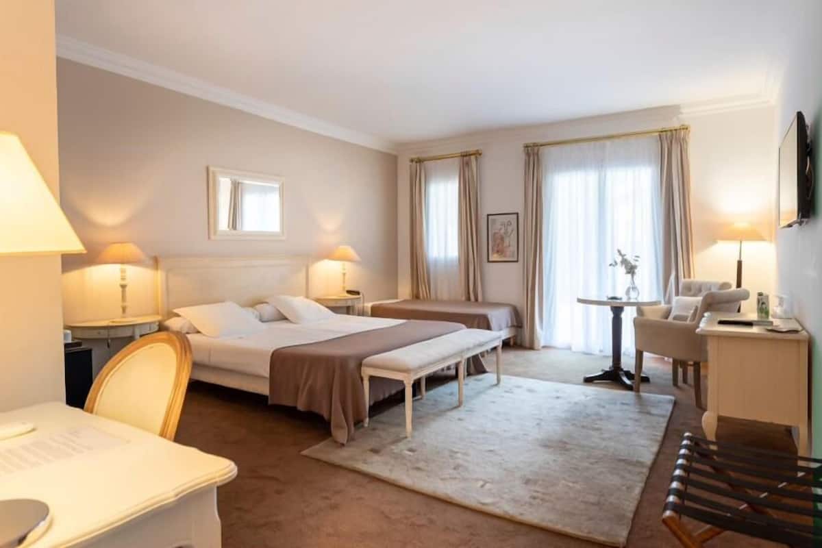 Habitación de hotel con una cama, dos mesitas de noche, un escritorio, una silla y una pequeña mesa con lámpara.