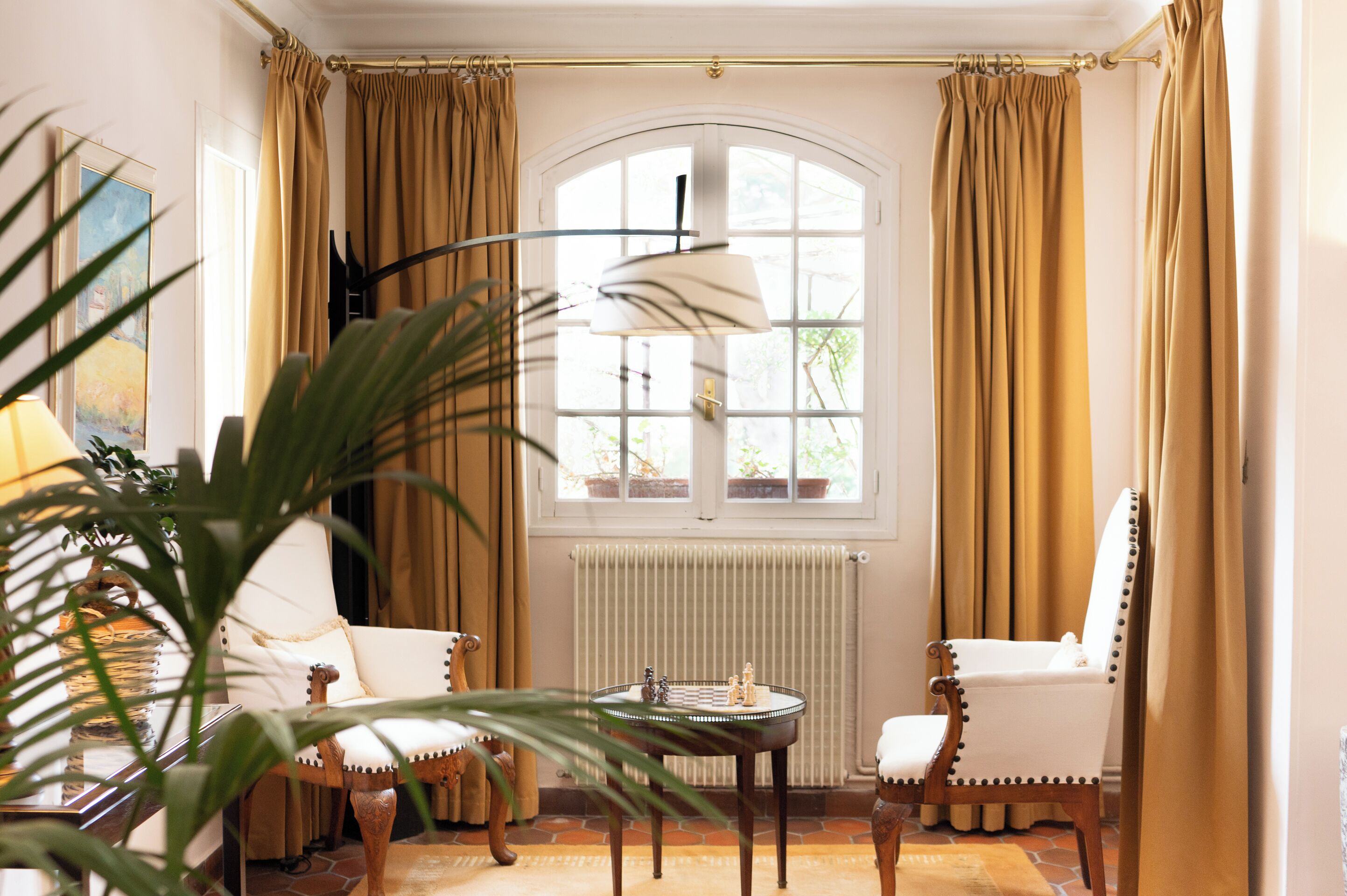 Una habitación con un ventanal grande, dos sillas, una mesa con piezas de ajedrez y un radiador.