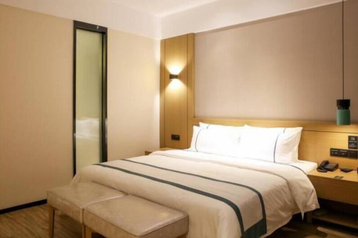 Ein Hotelzimmer mit einem Bett, Nachttisch, Lampe und einer Bank.
