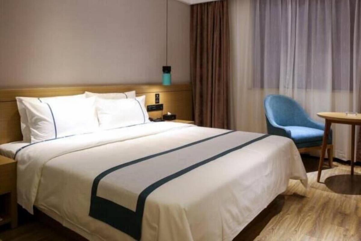 Ein Hotelzimmer mit Bett, Nachttisch, Schreibtisch, Stuhl und einem fenster mit Vorhängen.