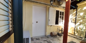 A narrow outdoor corridor with a white door, a window with shutters, and a small table with a barrel. - Cozy vacation apartment Panorama2 (Eretria)