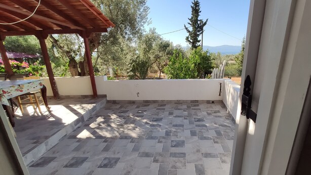 Une terrasse couverte avec un sol carrelé, une pergola en bois et une vue sur les arbres et les montagnes.