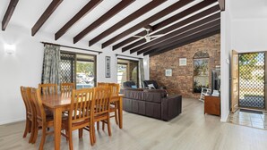 A dining area with a wooden table and chairs, a sofa, and a TV in a room with exposed wooden beams and brick walls. - Pet Friendly / Stroll to the beach (WOORIM)