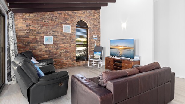 A living room with a brick wall, a black leather sofa, a brown leather couch, a TV, and a wooden cabinet. - Pet Friendly / Stroll to the beach (WOORIM)