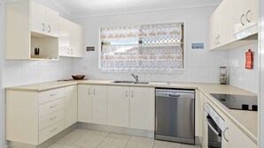 A modern kitchen with white cabinets, a dishwasher, an oven, and a window with patterned curtains. - Pet Friendly / Stroll to the beach (WOORIM)