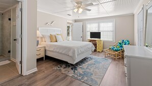 A bedroom with a bed, a desk, a chair, a ceiling fan, and a TV. - Byrd's Nest is located across the street from the beach and sleeps 10 (St Simons Island)
