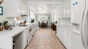 A kitchen with white cabinets, a dining area with a chandelier, and a refrigerator with blue stickers. - Byrd's Nest is located across the street from the beach and sleeps 10 (St Simons Island)