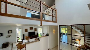 Een ruim, modern interieur met een hoge plafond, een eetgedeelte met een lange houten tafel en stoelen, een keuken met een inbouwoven, en een trap naar een hoger niveau.