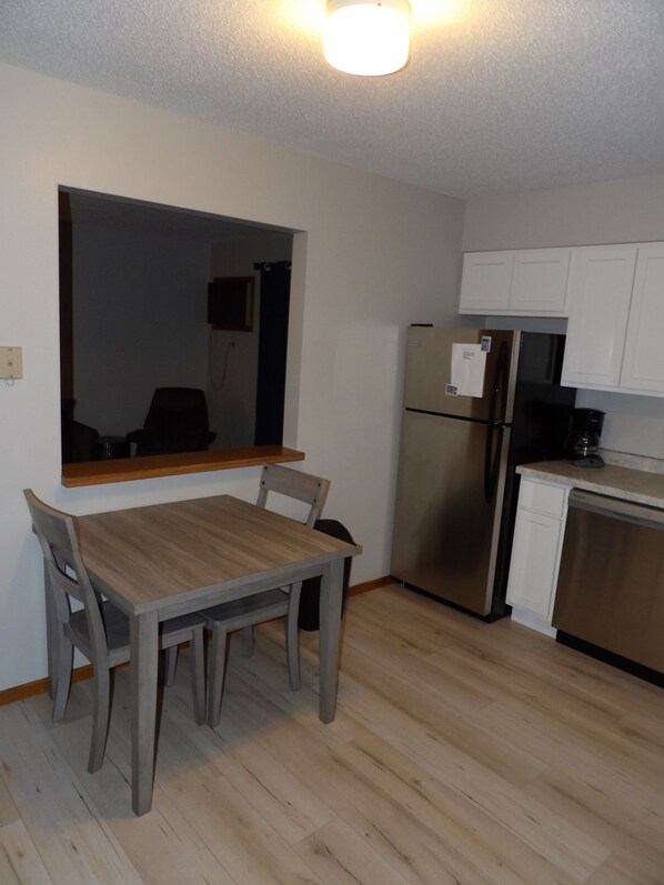 A compact kitchen with a dining table and chairs, a refrigerator, and a dishwasher. - Updated Suite in great location close to Bayfield, the Apostle Islands, and more (Washburn)