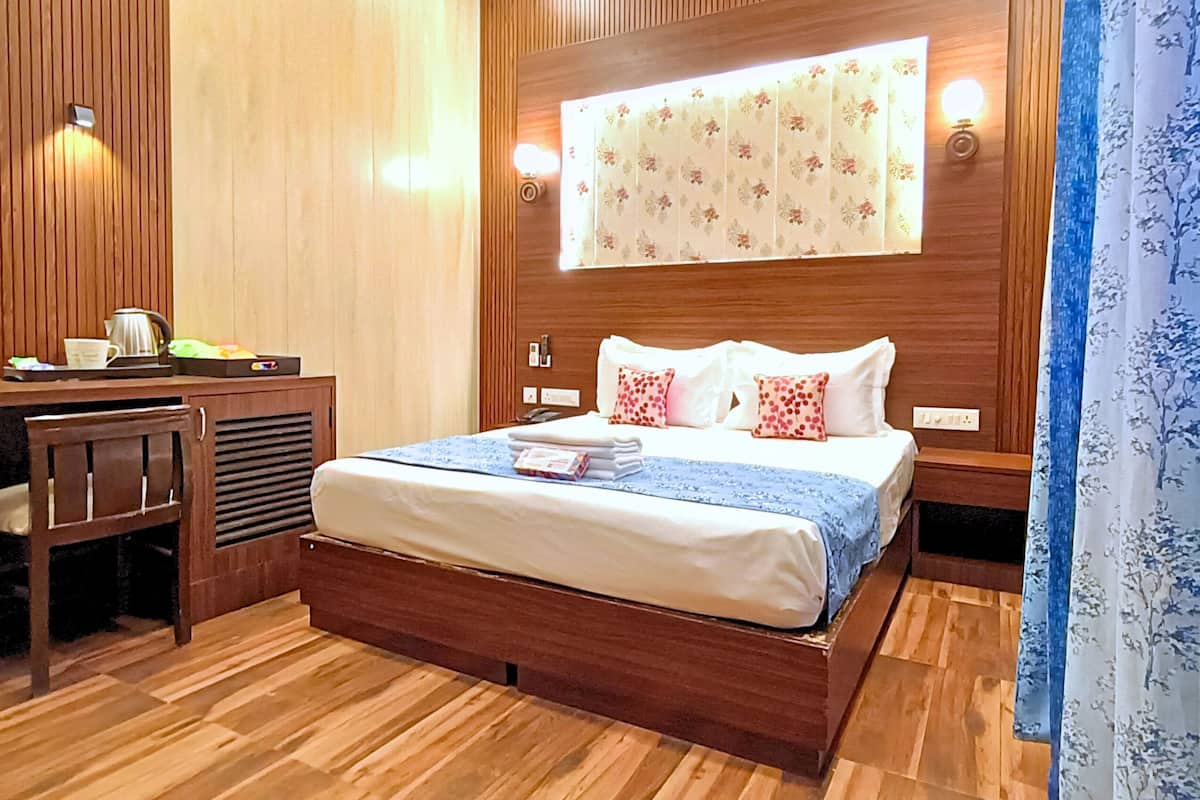 Habitació d'hotel amb llit de fusta, escriptori amb cadira, tauleta de nit i finestra amb cortines florals.