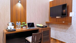 Une chambre d’hôtel avec un bureau en bois, un ordinateur portable, une bouilloire, deux bouteilles d’eau, une petite plante et un téléviseur fixé au mur.