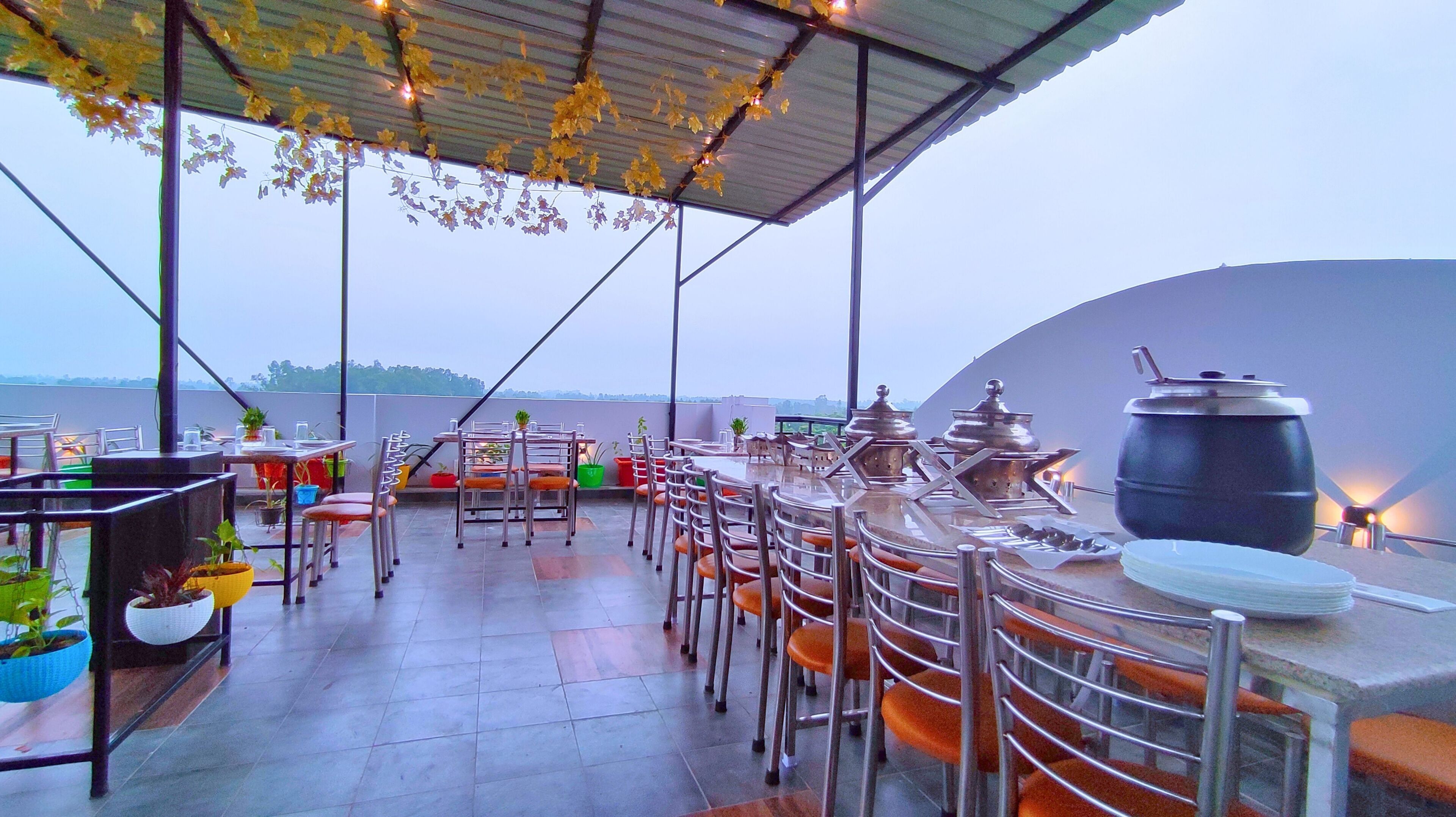 An outdoor dining area with metal chairs and tables, potted plants, and a large cooking pot.