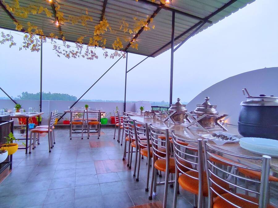 An outdoor dining area with metal chairs and tables, potted plants, and a large cooking pot.