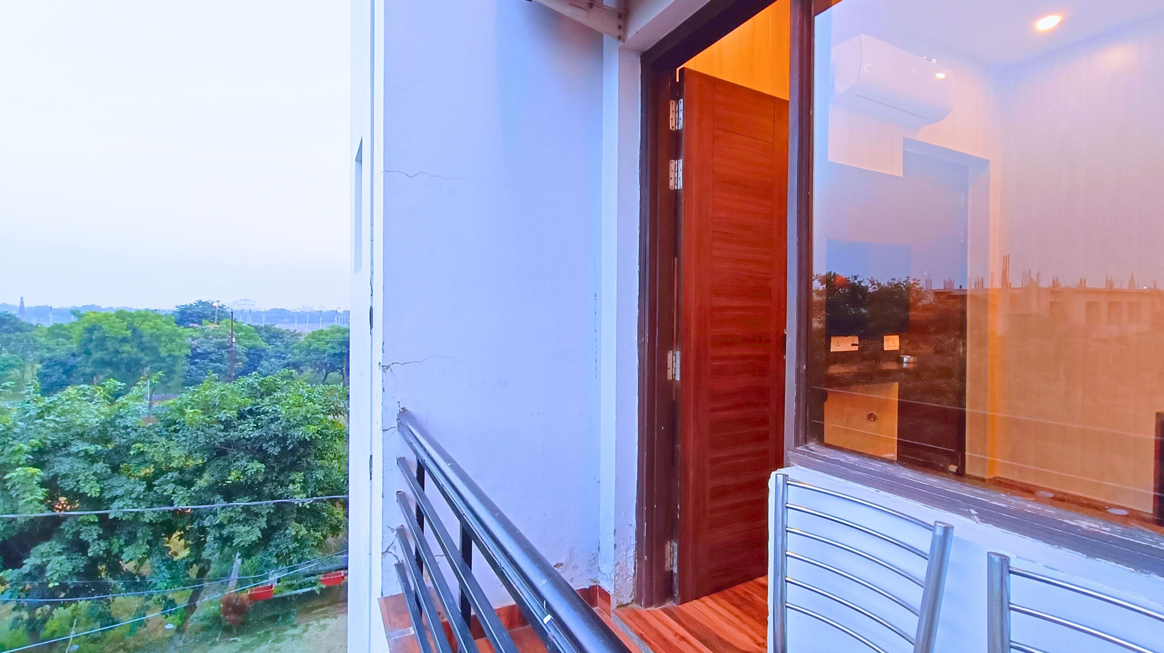A balcony with a wooden floor, a metal railing, and a view of greenery and buildings in the distance.