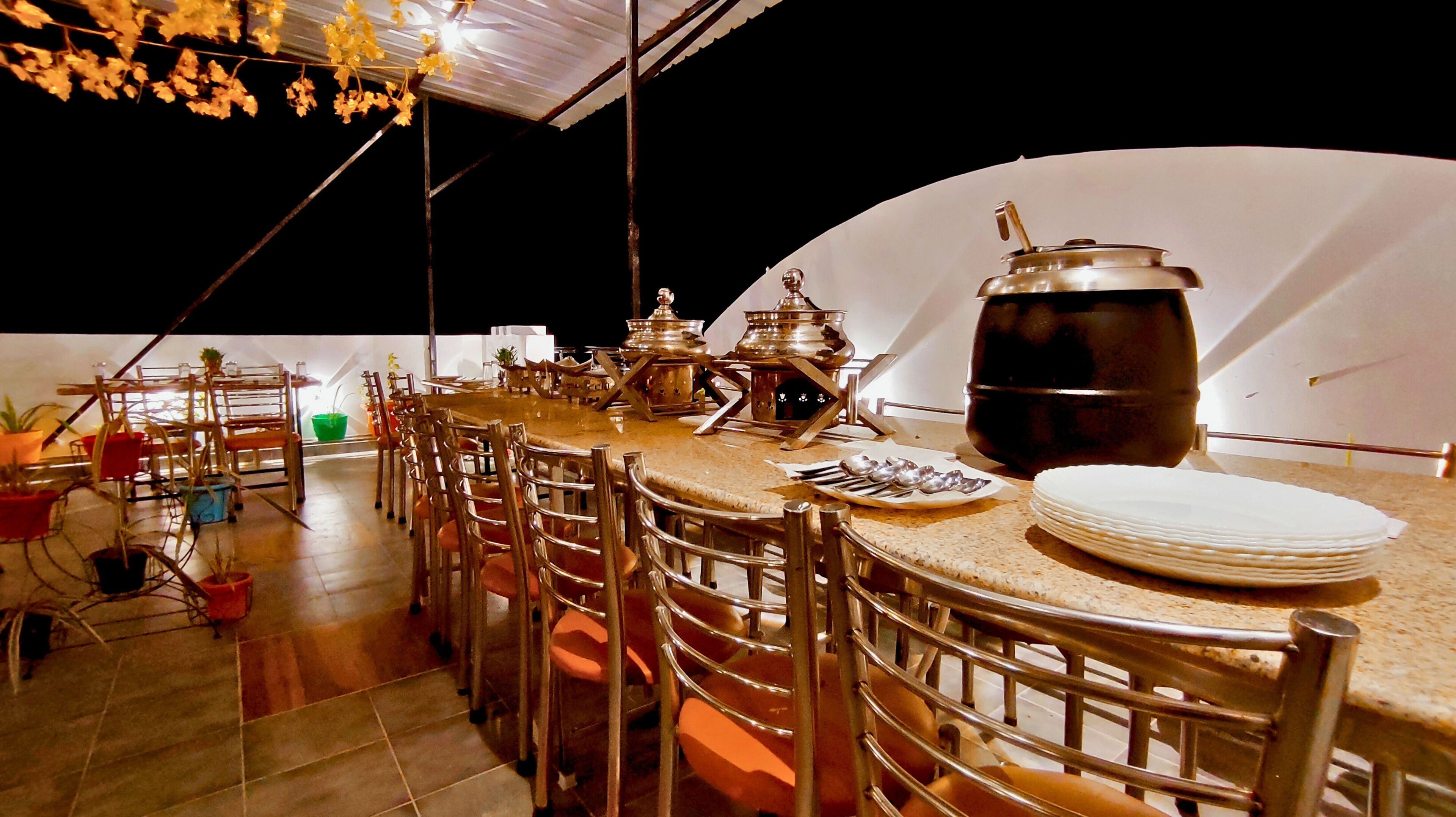 Un área de comedor al aire libre con una mesa larga, sillas y una olla grande sobre la mesa.