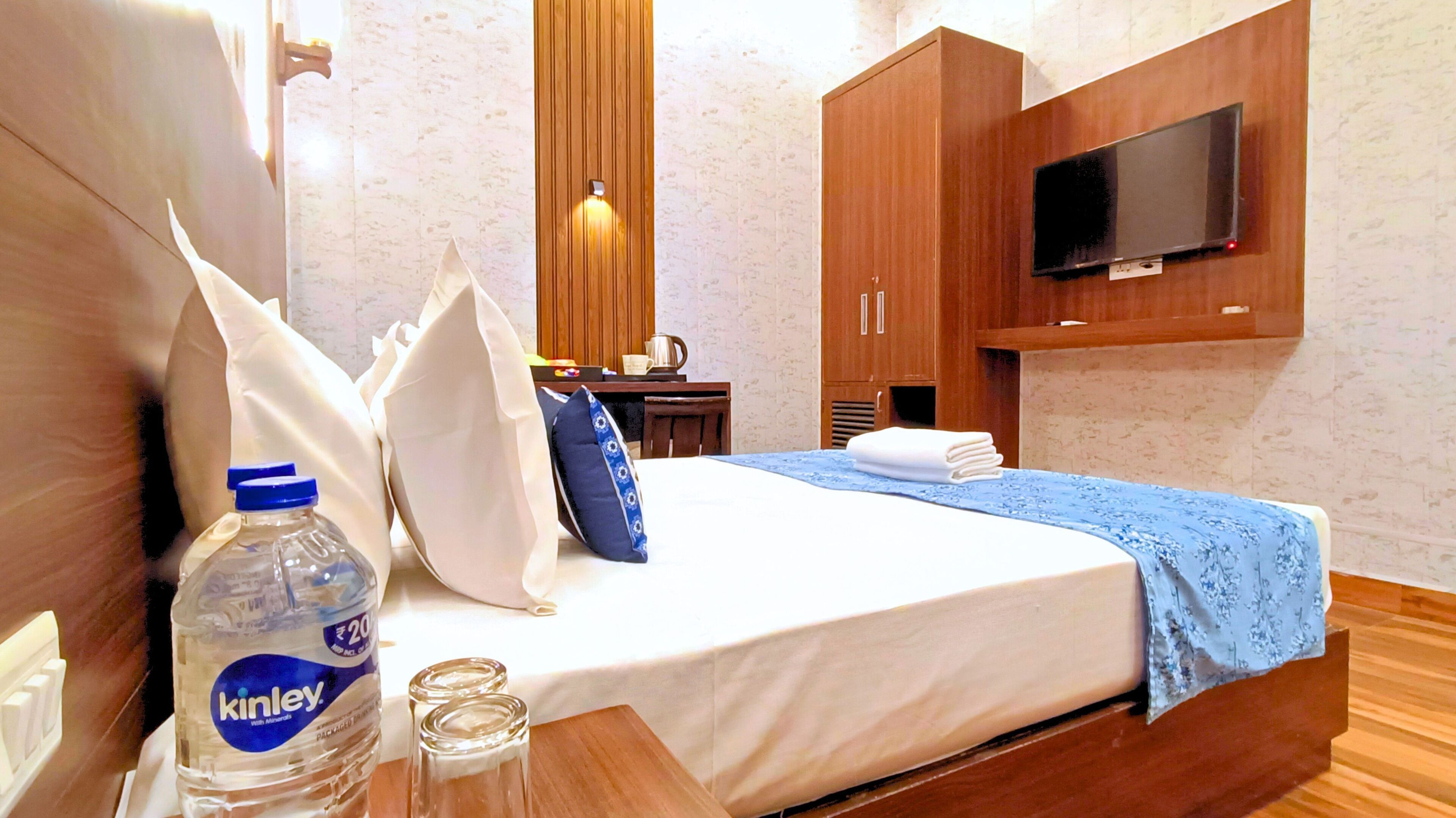 A hotel room with a bed, a TV mounted on the wall, wooden furniture, and a bottle of Kinley water.