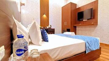 A hotel room with a bed, a TV mounted on the wall, wooden furniture, and a bottle of Kinley water.