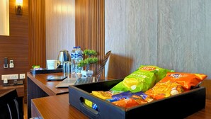 Un comptoir d’accueil d’hôtel avec un ordinateur portable, une bouilloire, une tasse à café, une plante et des en-cas.
