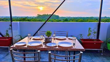 Una mesa para cuatro con platos, cubiertos y copas en un balcón con vistas a un paisaje boscoso.