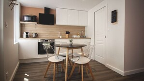 A compact kitchen with white cabinets, a wooden countertop, a black microwave, a stove, and a dining table with four chairs. - ♥♥ La Cachette Rouge ♥♥ (saint valery sur somme)