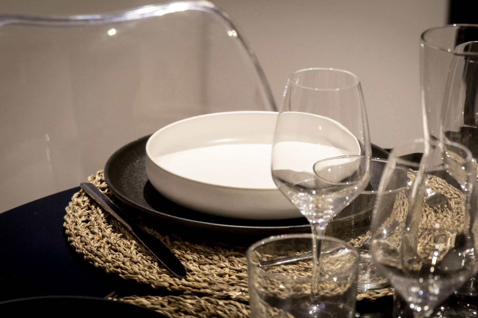 A table set with a white plate, a fork, and multiple wine glasses on a woven placemat.