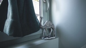 A towel hanging on a door handle, a small decorative elephant figurine on a windowsill, and a window with a view of greenery outside. - ♥♥ La Cachette Rouge ♥♥ (saint valery sur somme)