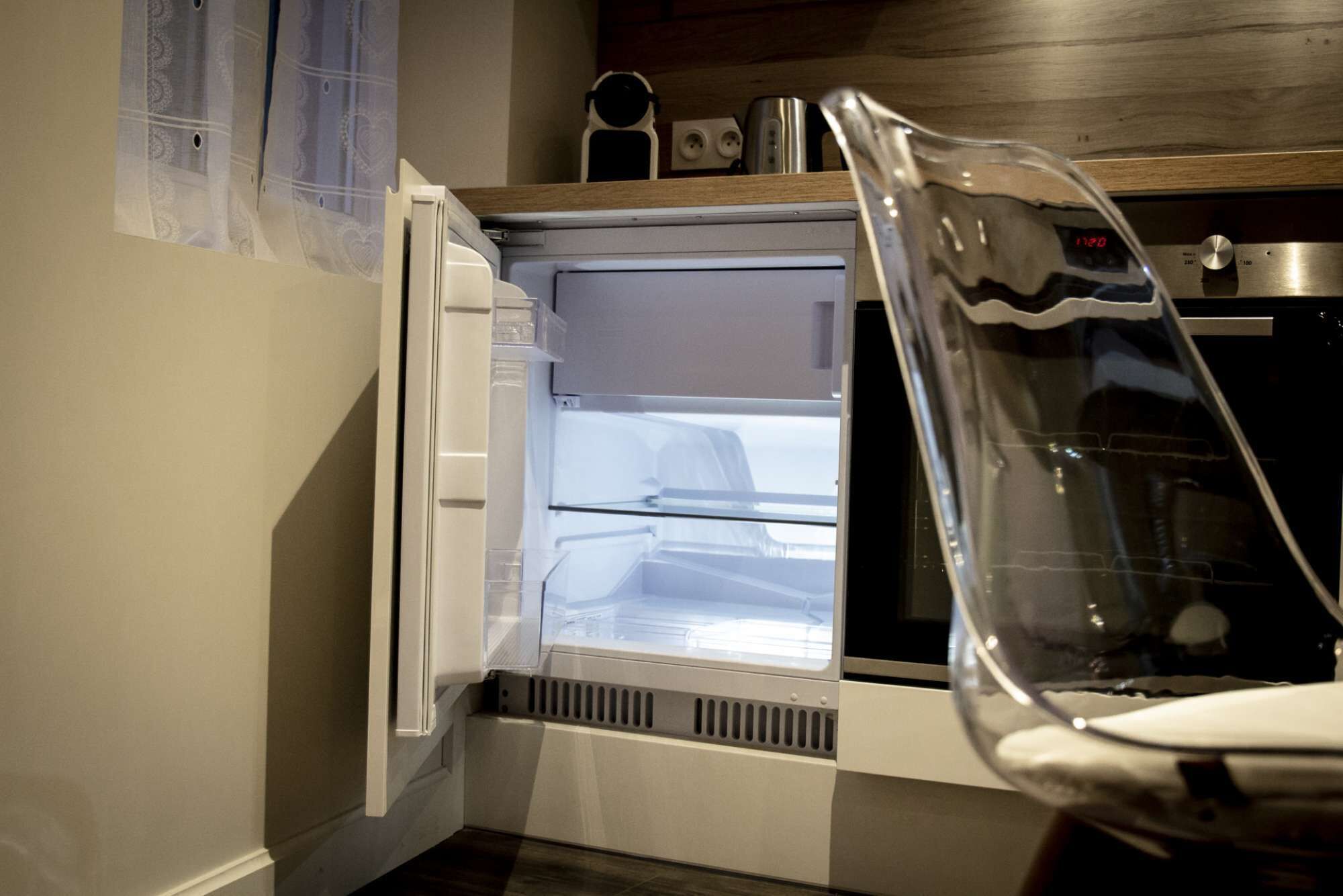 Une cuisine équipée d’un réfrigérateur et d’un four encastrés, d’un plan de travail en bois et d’une fenêtre avec un rideau.