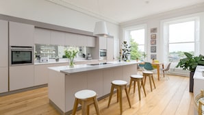 A modern kitchen with a central island, wooden stools, and a dining area with chairs and a table. - Crescent House (Edinburgh)