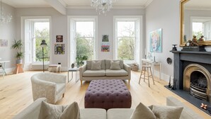 A spacious living room with a large window, a fireplace, and a chandelier. - Crescent House (Edinburgh)